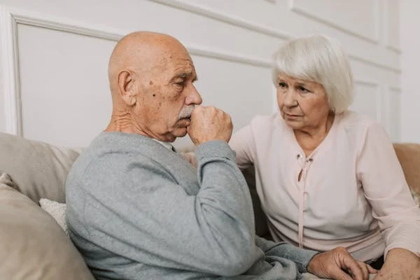Older adult coughing on couch