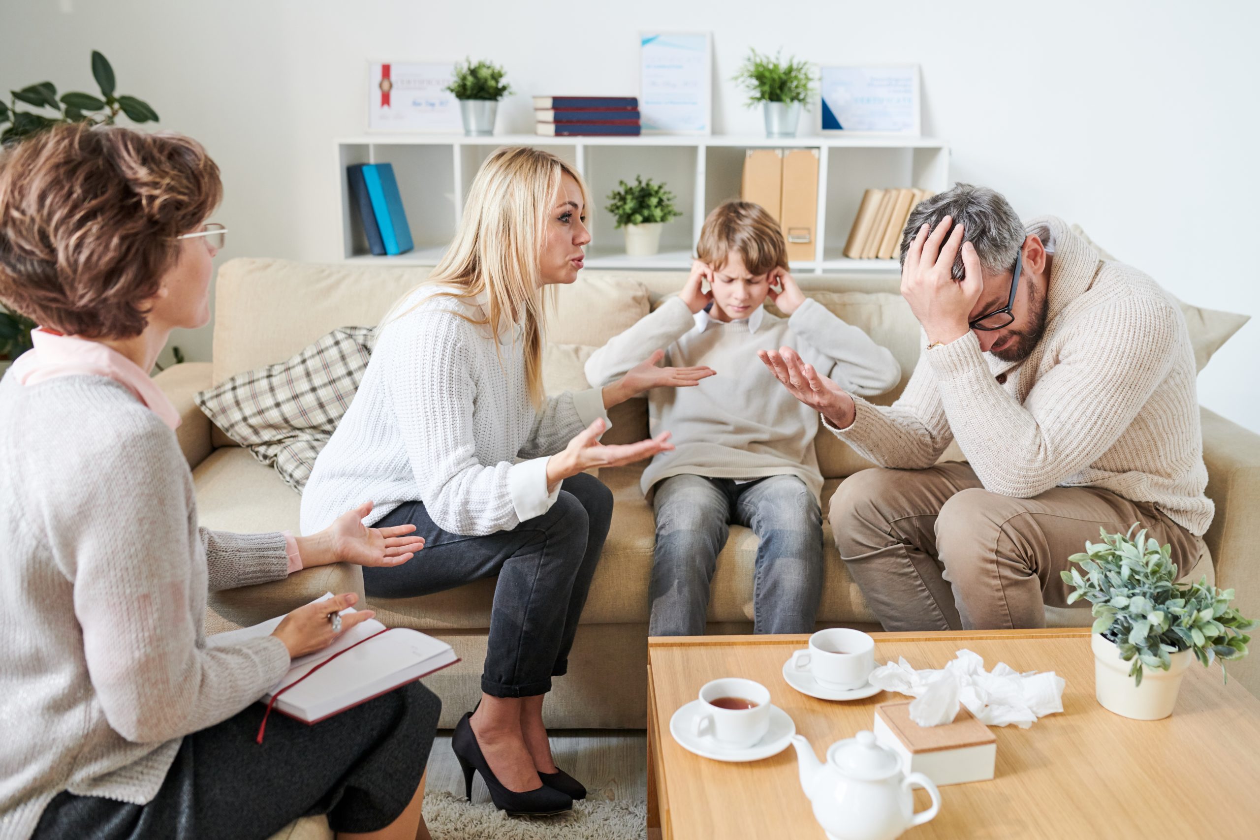 Sad son covering ears while parents having quarrel at therapy sessions